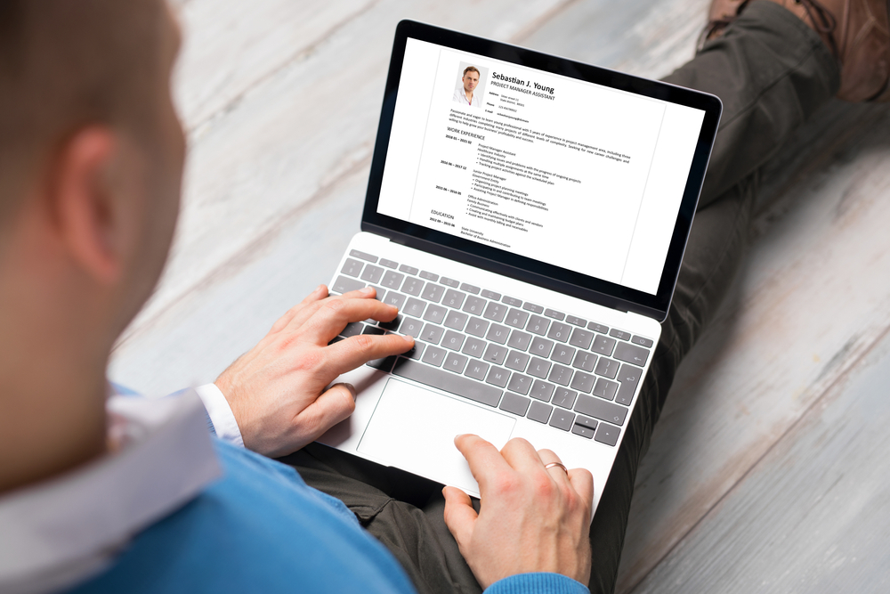 A man reviewing a professional CV on a laptop screen while sitting on the floor — showcasing resume layout quality from ParadigmResume, a trusted Toronto Resume Writing Service offering expert CV Writing Services.