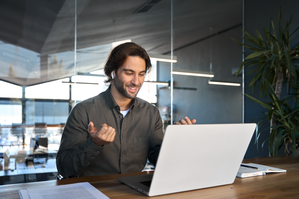 Man smiling while participating in a video meeting on a laptop in a modern office.