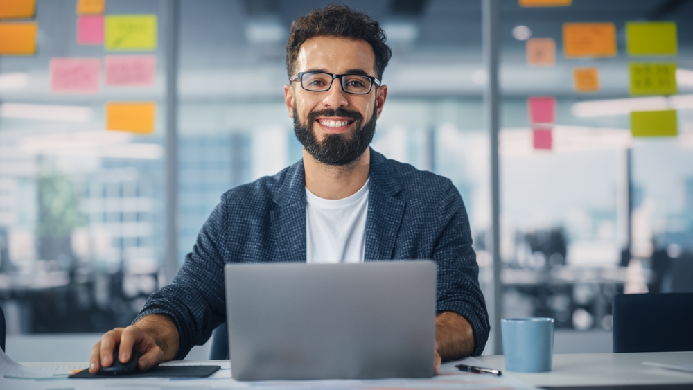 Smiling office worker typing at a laptop in a modern workspace.