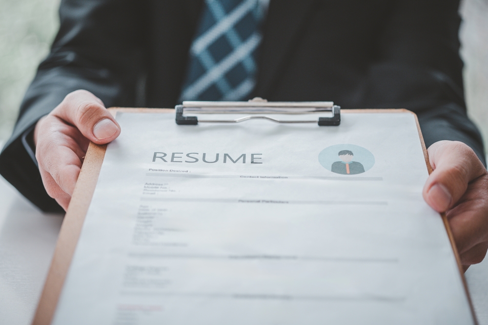 Person holding a resume on a clipboard during a job application review.