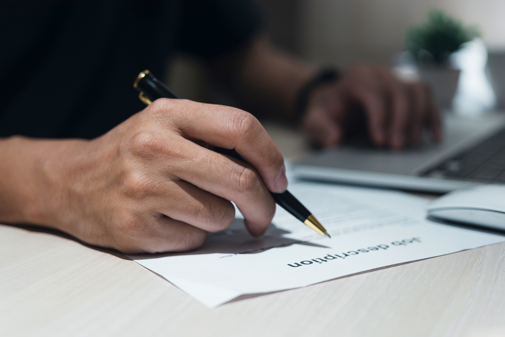 Person signing a resume document at a desk with a laptop.