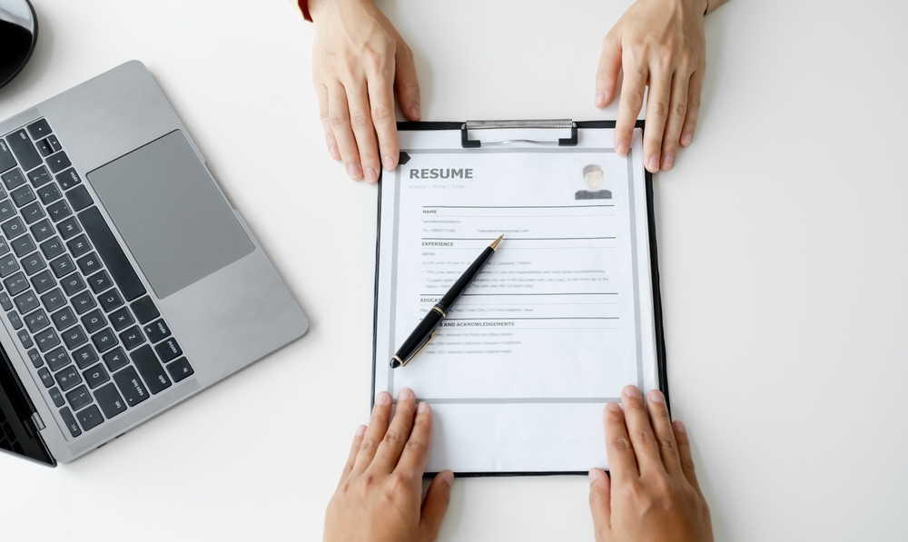 Hands presenting a printed resume on a clipboard during a professional discussion