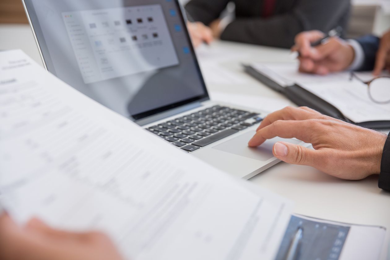 Hands working on a laptop beside printed documents
