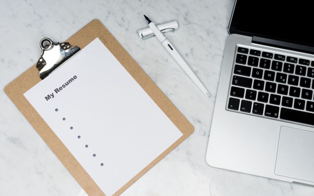 Printed resume on a clipboard beside a laptop and pen